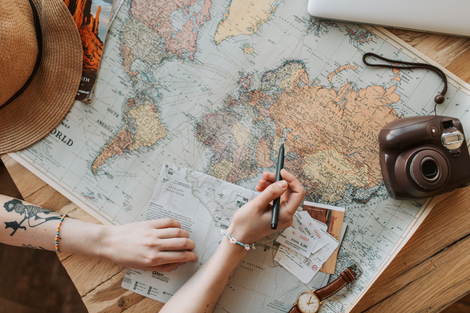 Top view of a woman's hands planning a trip with a map, camera, and travel items