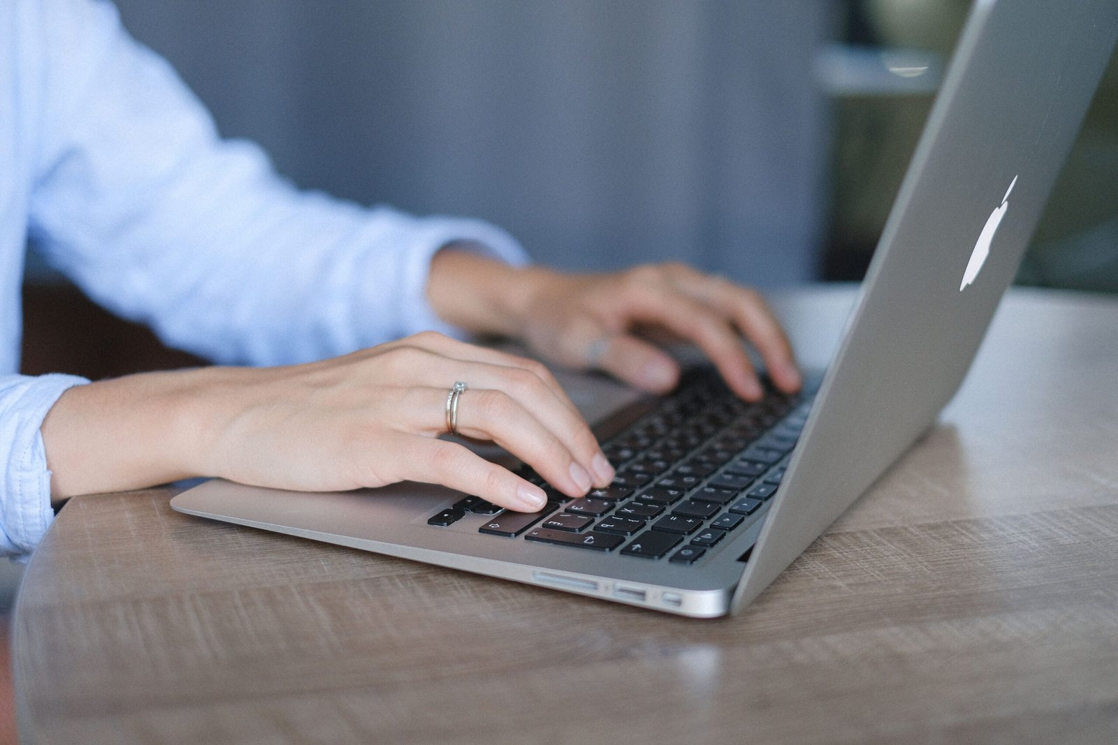 Seorang wanita mengetik di laptop di meja kayu