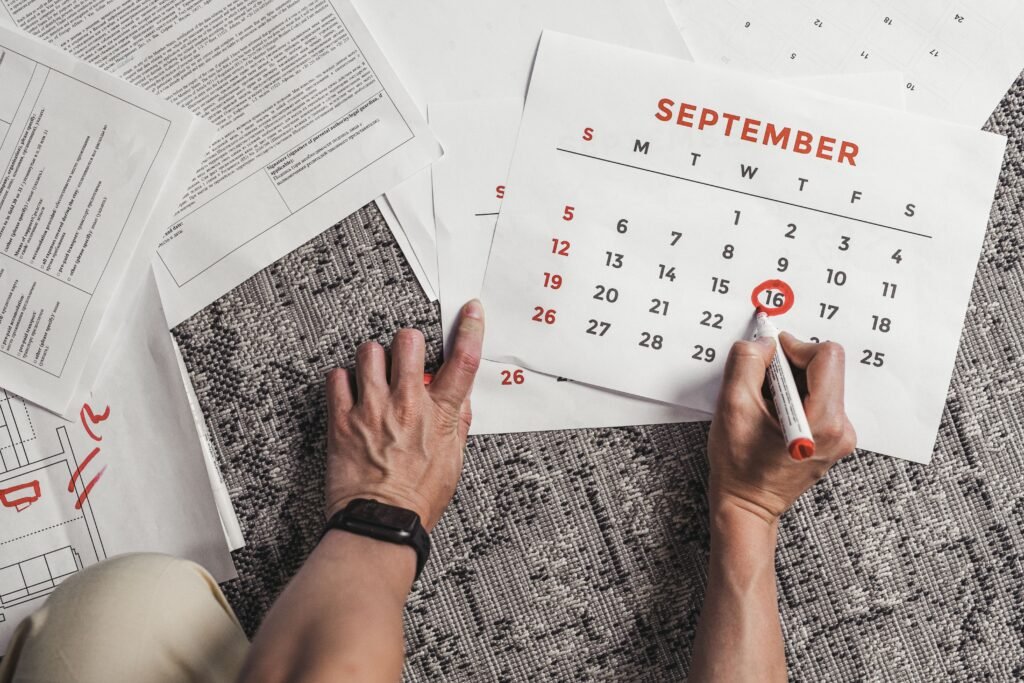 Tangan memegang kalender dengan tanggal September yang dilingkari, dikelilingi oleh dokumen di atas karpet