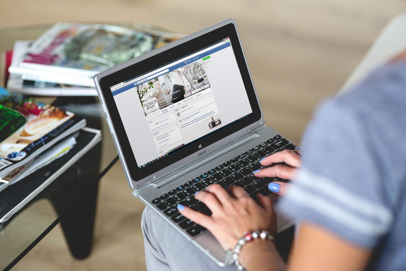 Seorang wanita sedang mengetik di laptop dengan tampilan facebook di layar