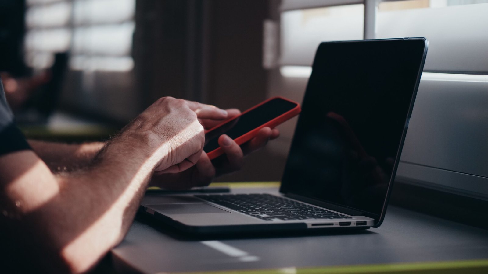 A person holding a smartphone near a laptop in an indoor setting