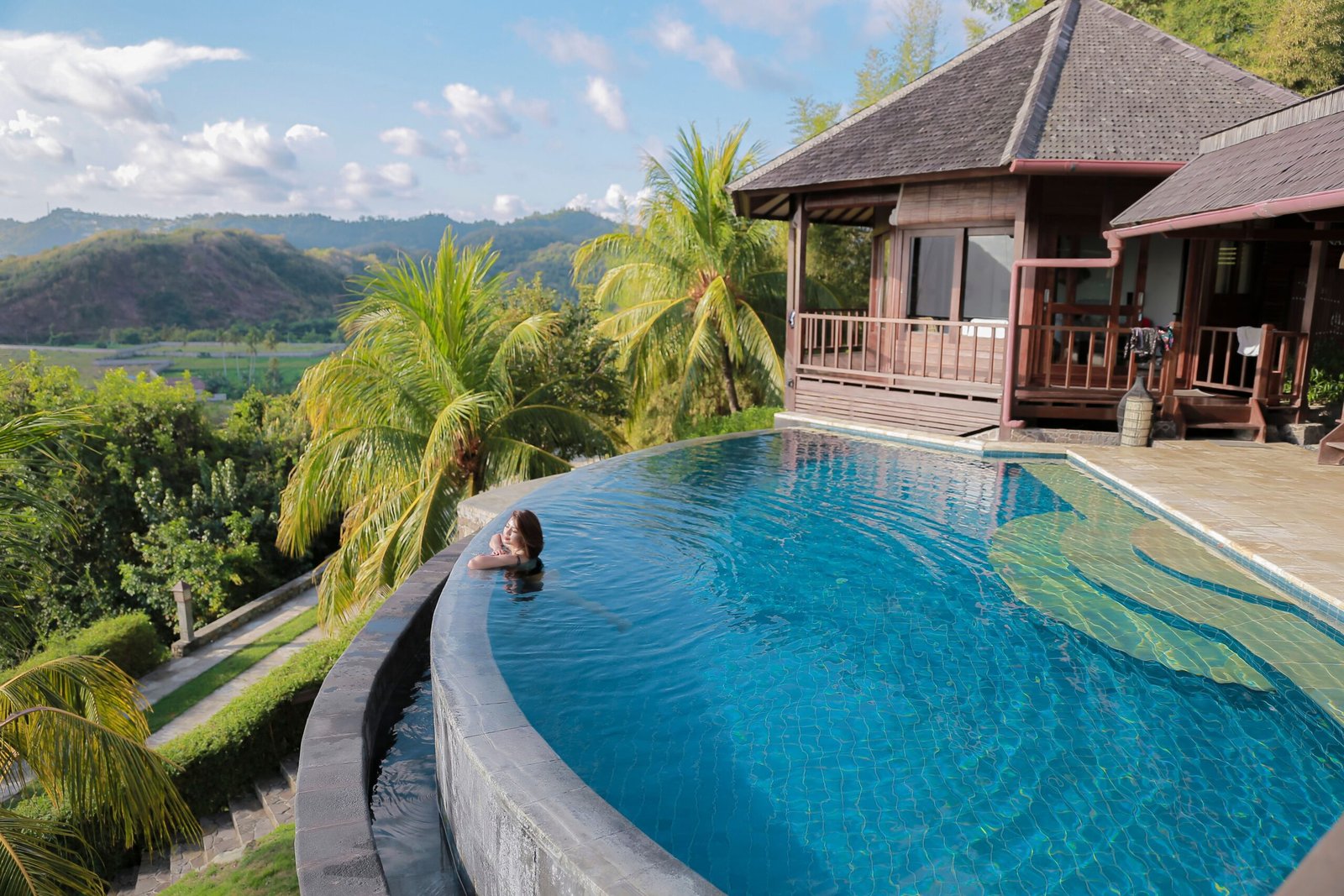 A woman relaxes in an infinity pool overlooking tropical scenery at a Bali villa