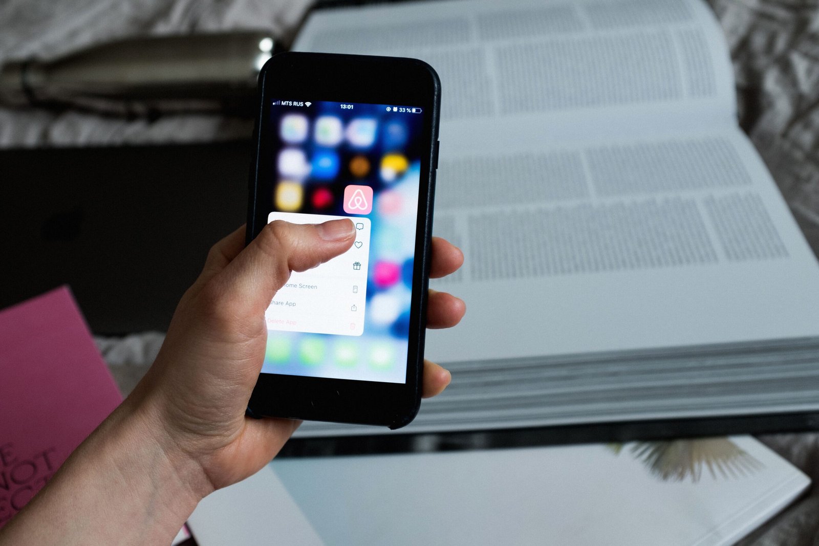 Hand holding a smartphone above an open book with a mobile app displayed on screen. 
