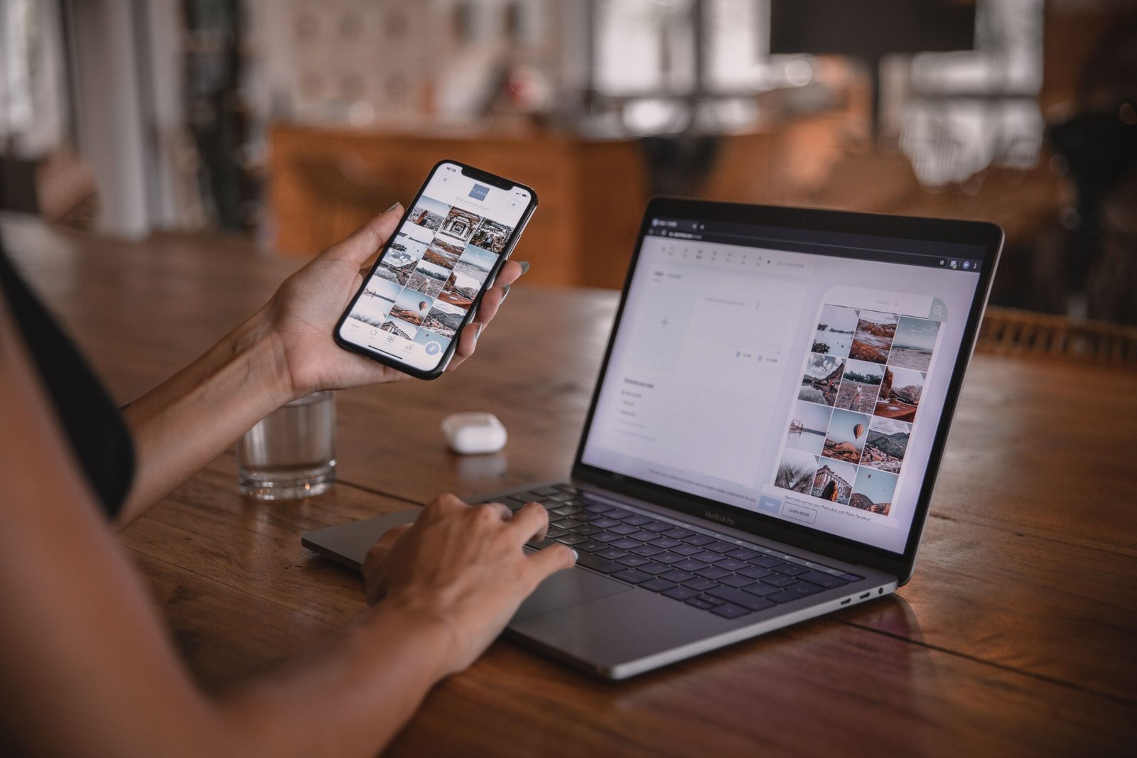 Person planning an Instagram content feed on a smartphone and laptop at a wooden table