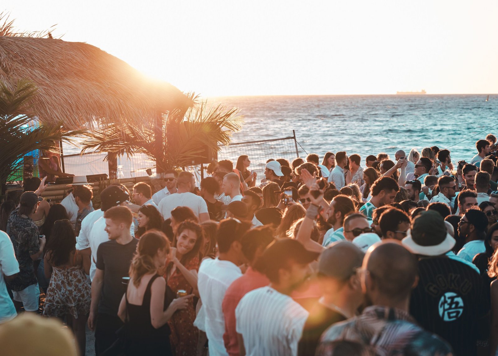 Crowd of guests enjoying a sunset party at a beach club with a thatched bar and ocean view