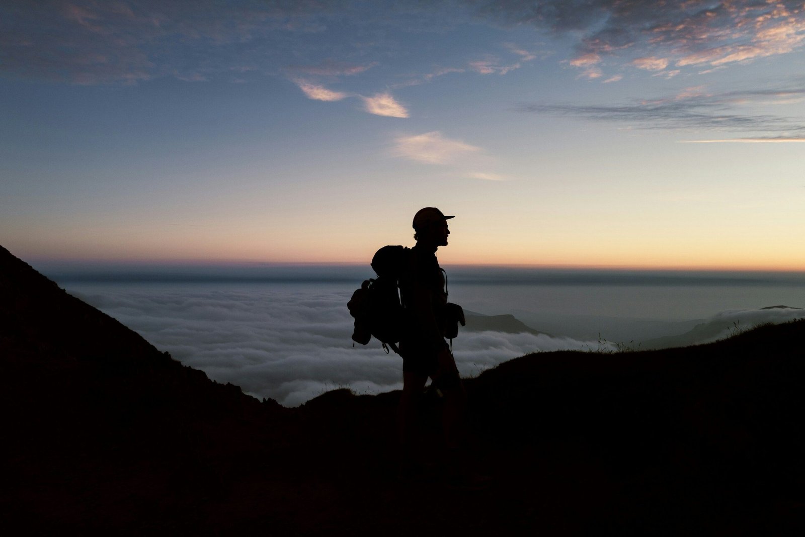 A lone hiker stands silhouetted against a stunning sunrise sky on a mountain peak