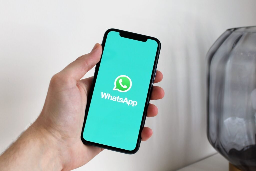 Tampilan dekat tangan yang memegang ponsel pintar yang menampilkan layar aplikasi WhatsApp