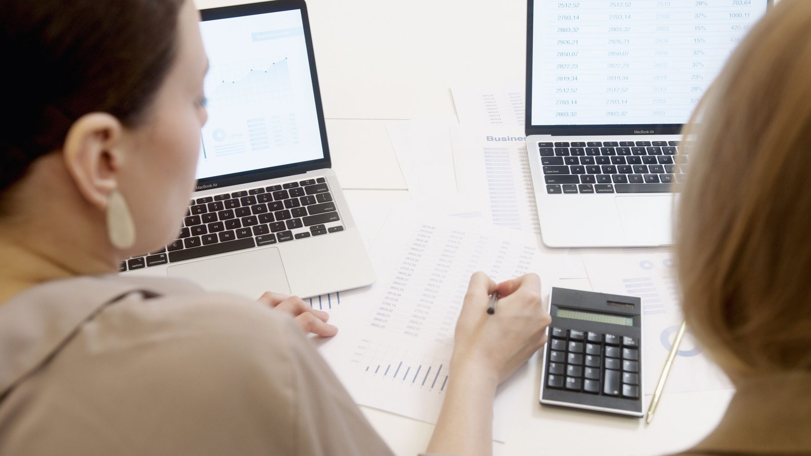 Dua orang menganalisis data spreadsheet di laptop dengan bagan dan grafik