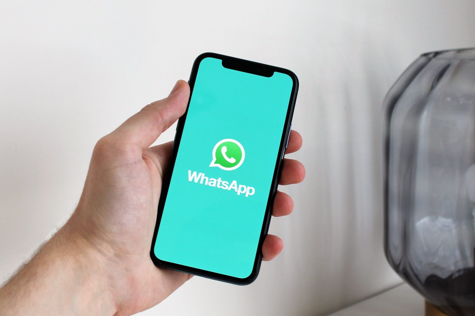 Tampilan dekat tangan yang memegang ponsel pintar yang menampilkan layar aplikasi WhatsApp
