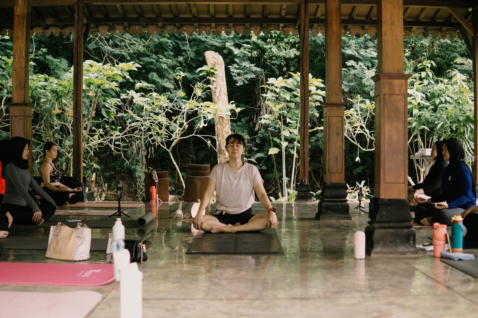 Group yoga class in an open-air studio surrounded by greenery in morning light